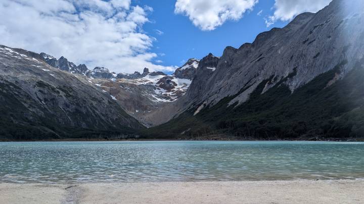 Turquoise glacial lagoon surrounded by steep snow-tipped peaks and forested slopes under a brilliant sky.
