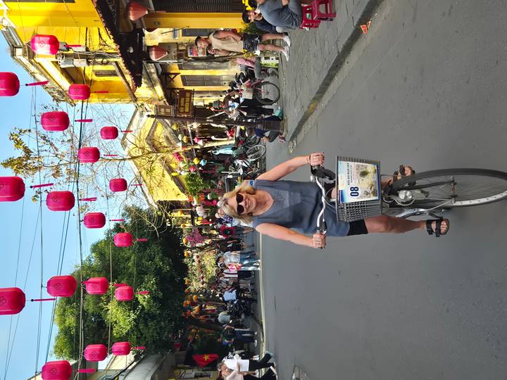 Cyclist glides beneath colourful lanterns hanging over a historic street at dusk.