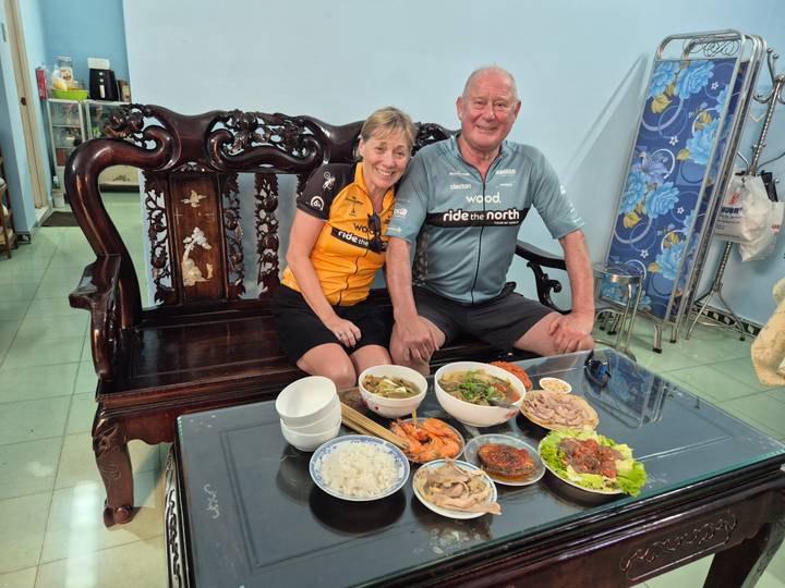 Couple seated indoors share a hearty Vietnamese meal laid out on low tableware.