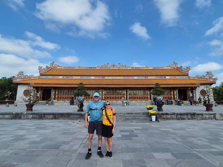 Travellers pose in the spacious forecourt of a richly decorated palace building within Hue Citadel.