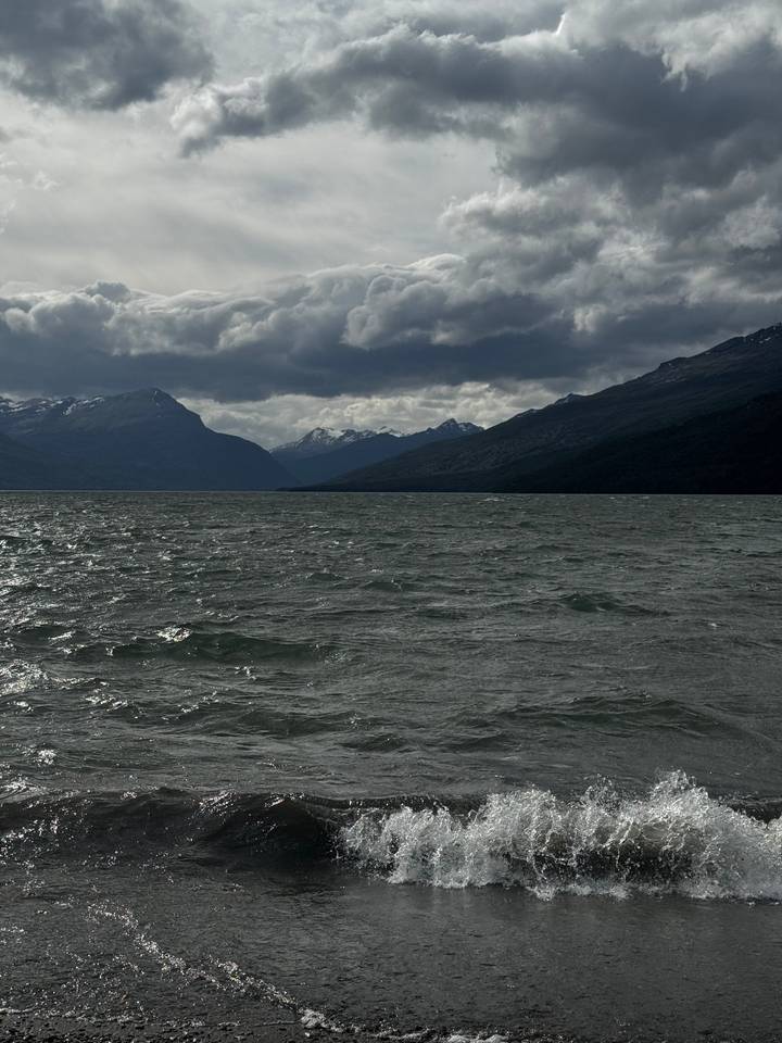 Wind-ruffled dark lake under brooding clouds with distant snowy peaks on the horizon.