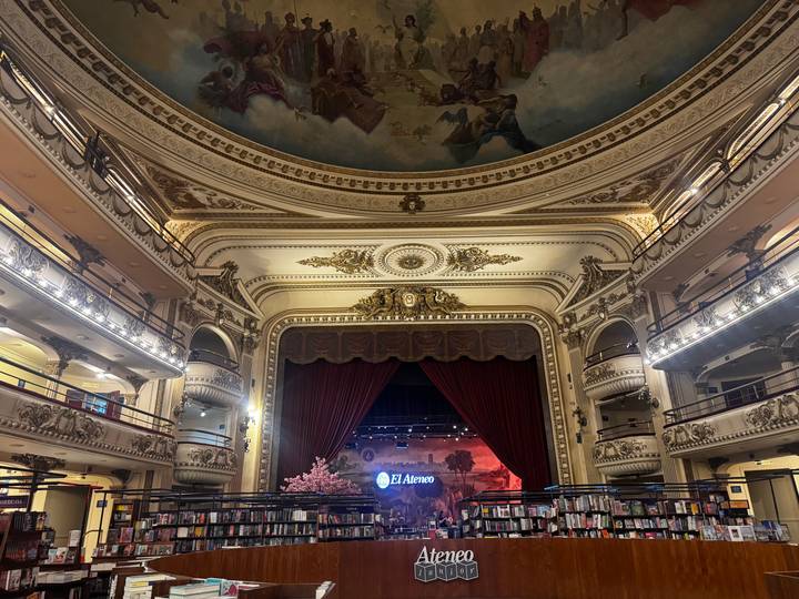 Opulent theater hall converted into a bookstore with ornate balconies, gilded décor, and a red stage curtain.