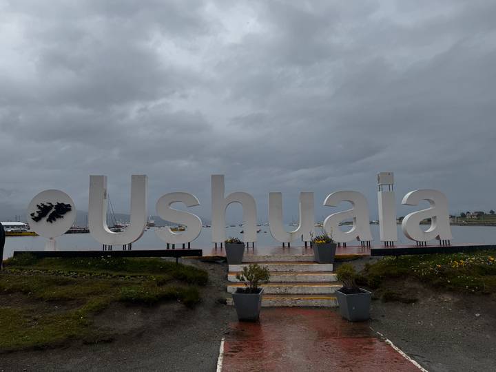 Silhouette of large Ushuaia letters against a grey sky by the harbor.