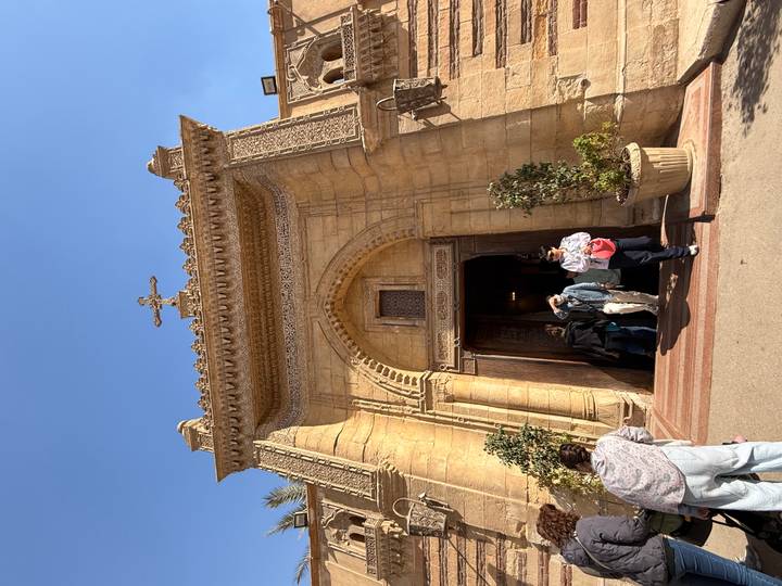 Stone façade of the Hanging Church entrance with visitors stepping through the arched doorway.