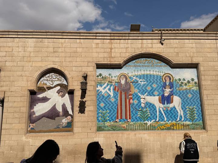 Colorful religious mosaics depicting biblical scenes on a stone wall under blue sky.
