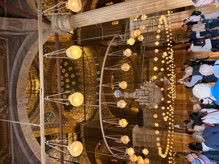 Lavish interior of the Muhammad Ali Mosque with hanging lamps and gilded domes crowded by tourists.