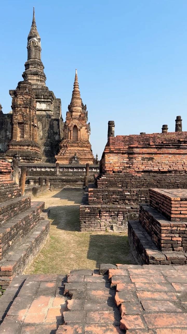 Ancient brick ruins and Buddha statues of Sukhothai Historical Park under clear skies.