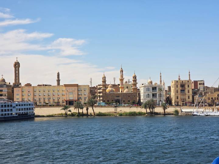 A skyline of sand-colored buildings and minarets along the Nile with blue river water in the foreground.