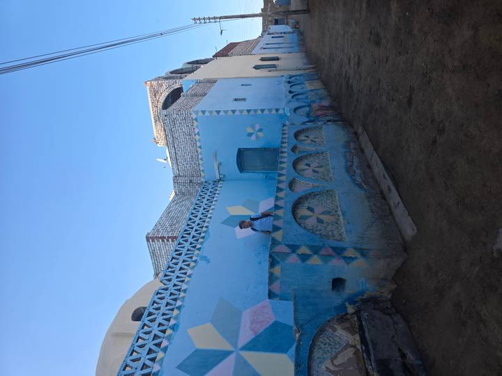 A traveler beside a blue-painted Nubian village wall adorned with star patterns under a bright sky.