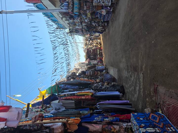 A quiet market lane lined with fabric stalls and overhead strings of bunting during daylight.