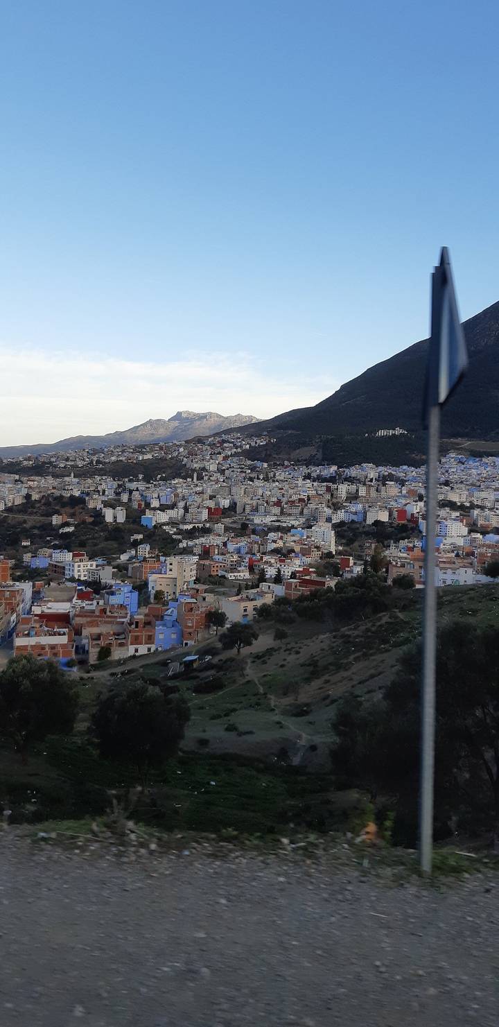A sprawling hillside city with clusters of blue and white buildings surrounded by mountains.