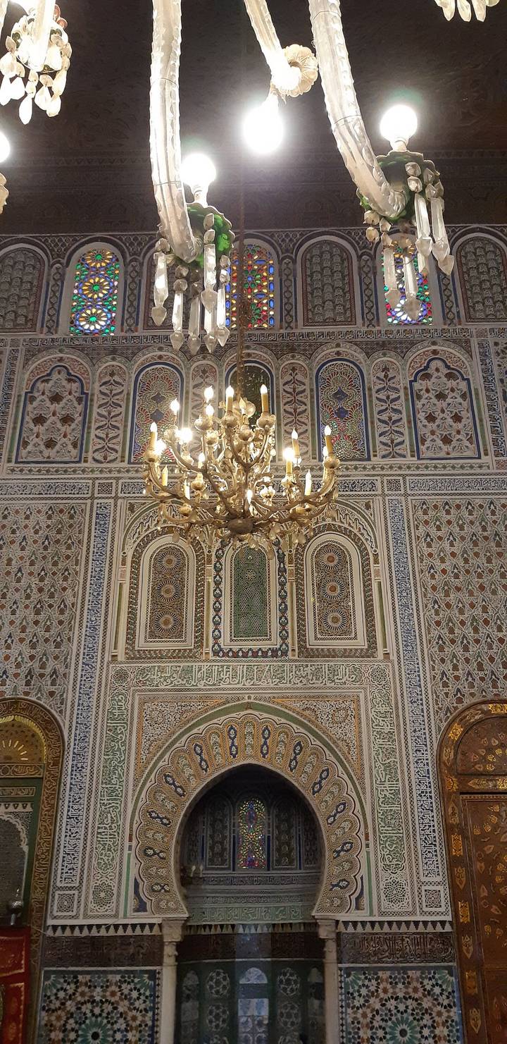 Close view of an elaborate chandelier set against mosaicked Moroccan walls and arches.
