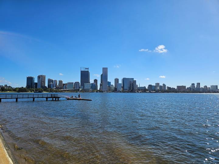 Cityscape of Perth across the blue Swan River viewed from a jetty on a sunny day.