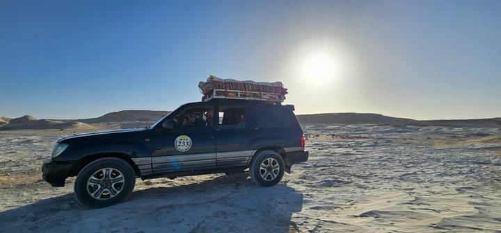 4x4 jeep with roof-rack drives across sun-bleached desert under bright sky