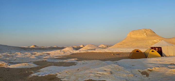 Yellow tents pitched beside chalky mounds in desert at warm dawn light