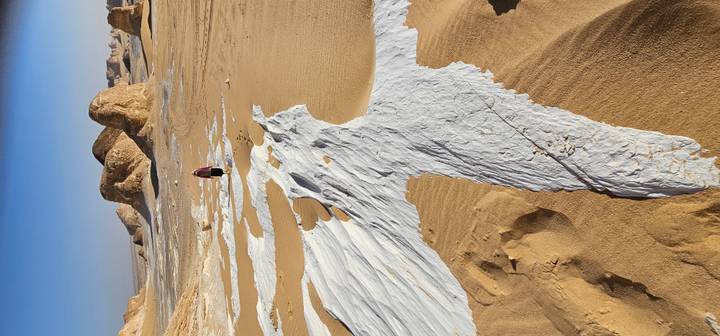 Person walks through striped white and tan desert terrain toward sandstone buttes