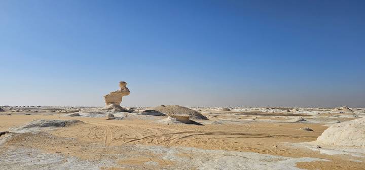 Isolated limestone pillar stands in vast flat desert beneath clear blue sky