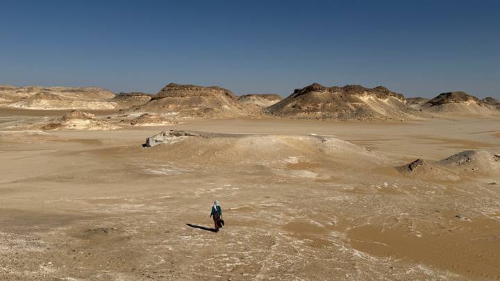 Single traveller dwarfed by expansive sandy plain and low rocky hills