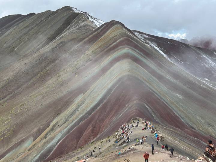 Multicolored striations of Rainbow Mountain with hikers trekking along the steep ridge in thin mountain air.
