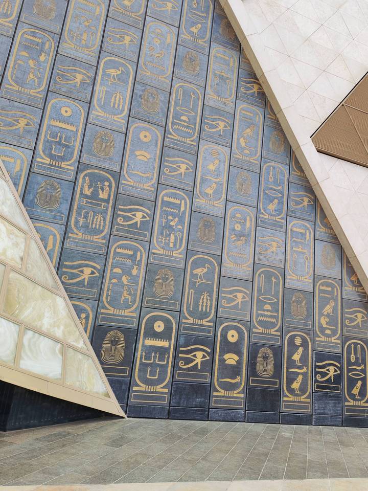 Decorative wall of blue stone inlaid with golden ancient Egyptian cartouches and symbols.