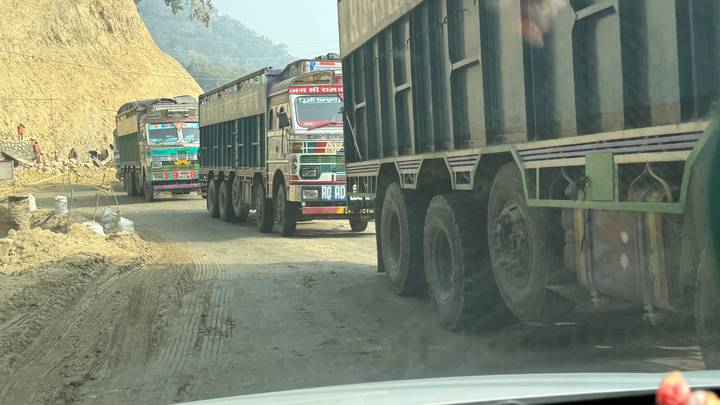 Colorful cargo trucks queue on a dusty mountain road construction zone.