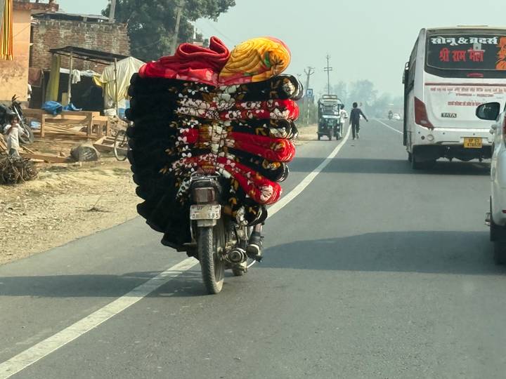 Motorcycle overloaded with stacked colourful blankets wobbling along a rural highway.