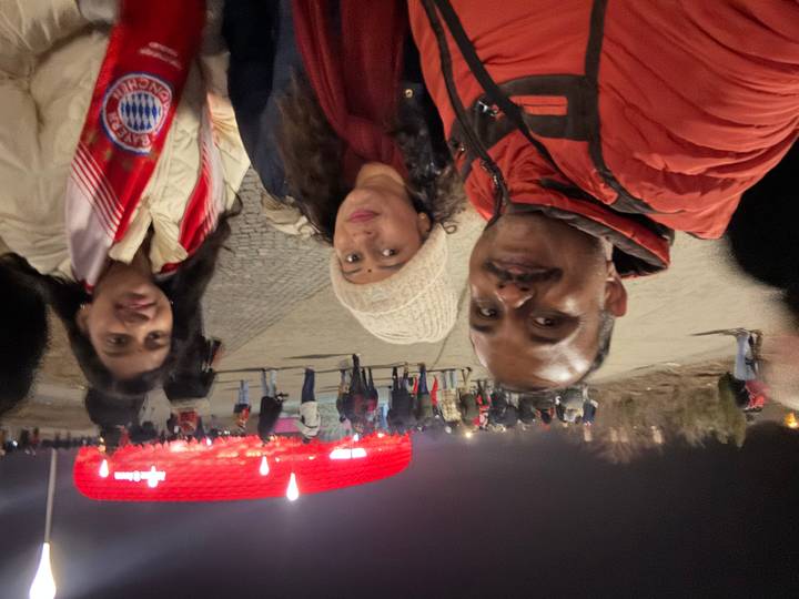 Family stands outside glowing red Allianz Arena with evening crowds.