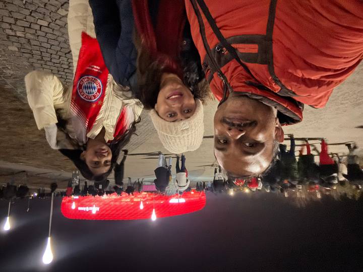 Night shot of family posing with Bayern scarves near Allianz Arena crowd.