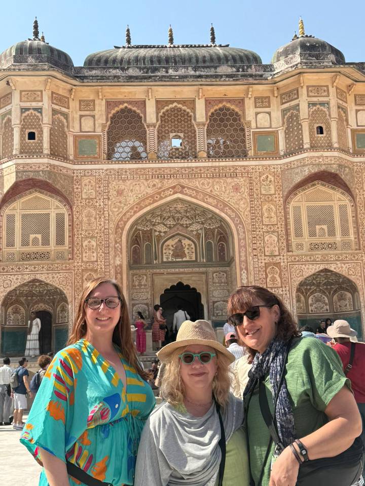 Two travellers smile in front of the ornate gateway of Amber Fort in Jaipur.
