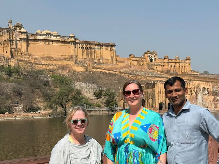 Travellers with local guide stand by a lake with Amber Fort sprawling across the hillside behind.