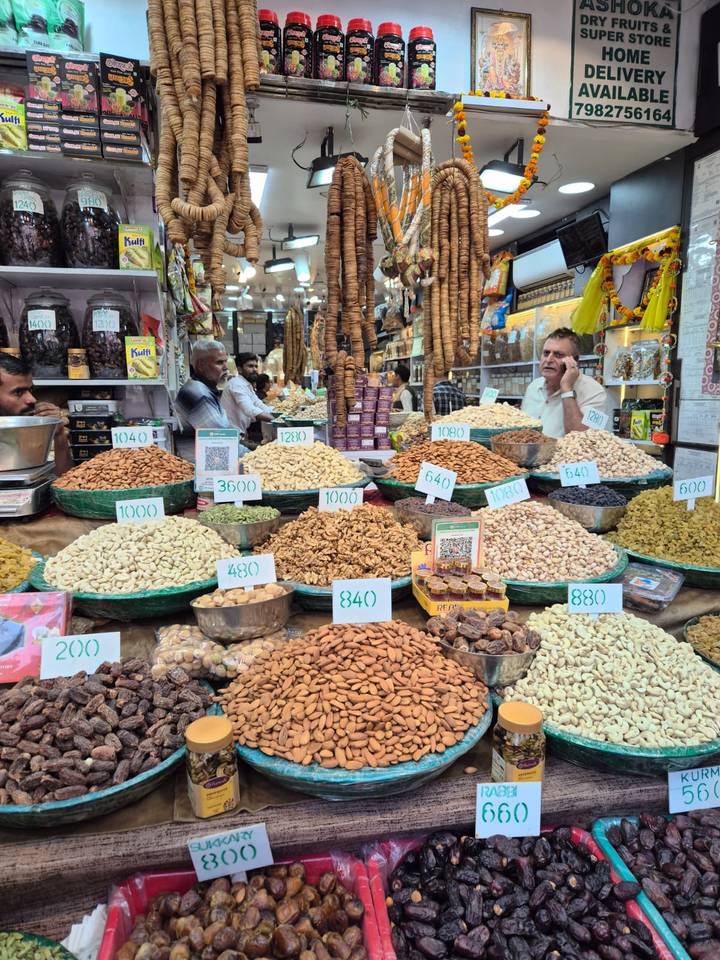 Bustling spice and nut stall with mounds of produce labelled by price in a crowded market.