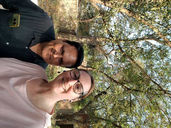 Selfie of tourist with local driver beneath leafy trees on a sunny afternoon.