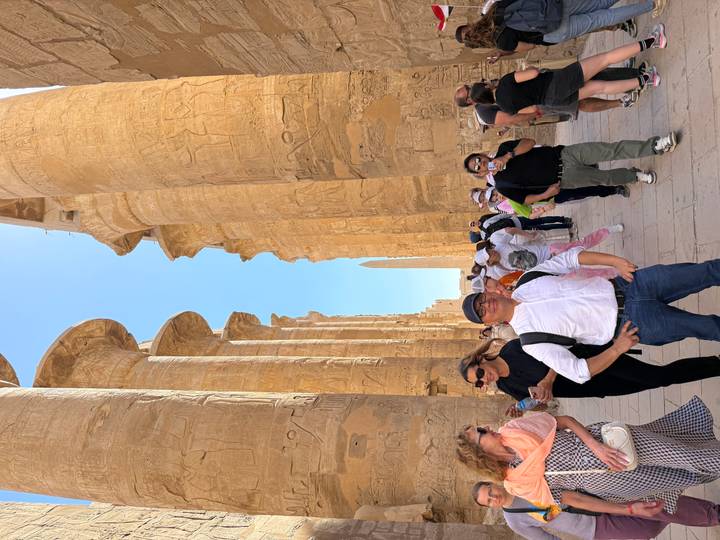 Crowd walks between massive hieroglyph-covered columns at Karnak Temple.