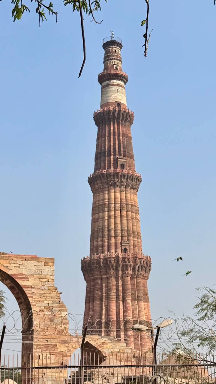Tall sandstone Qutub Minar tower rising against a clear blue sky