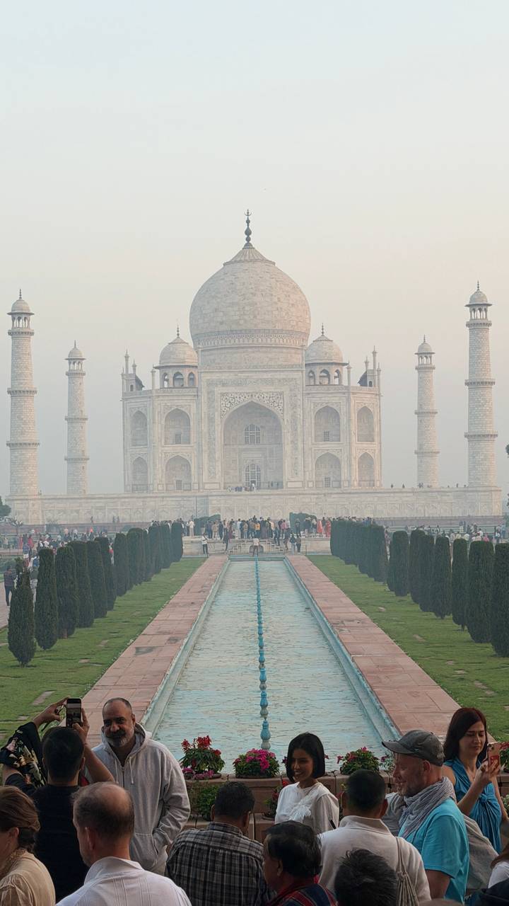 Front view of the Taj Mahal with reflecting pool and crowds of visitors in morning haze