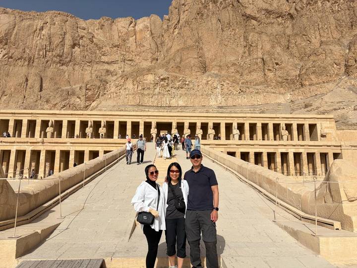 Visitors pose on the approach to the Mortuary Temple of Hatshepsut amid dramatic desert surroundings.