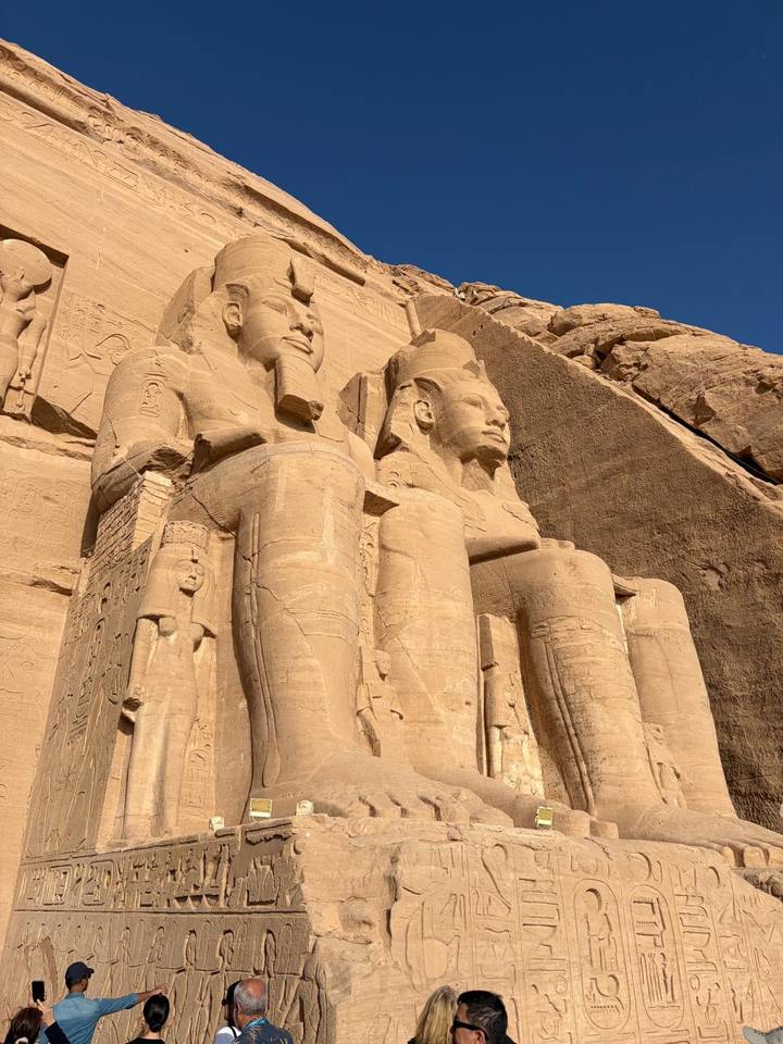 The towering sandstone statues at the entrance of Abu Simbel temple captured in bright light against a clear sky.