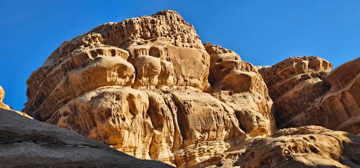 Close-up of dramatic golden sandstone cliffs rising under a clear blue desert sky.