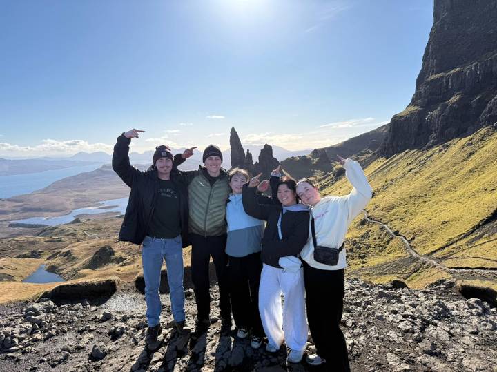 Five friends celebrate at the dramatic Old Man of Storr viewpoint overlooking the sea and cliffs.