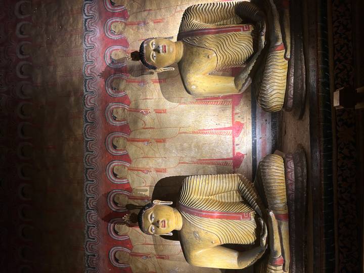 Row of illuminated Buddha statues inside a cave temple with intricate wall paintings