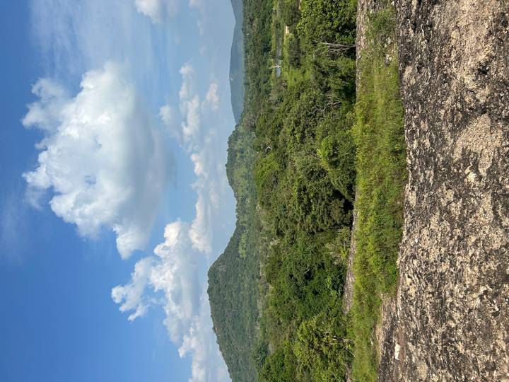 Expansive scrubland and rolling green hills beneath a bright blue sky with scattered clouds