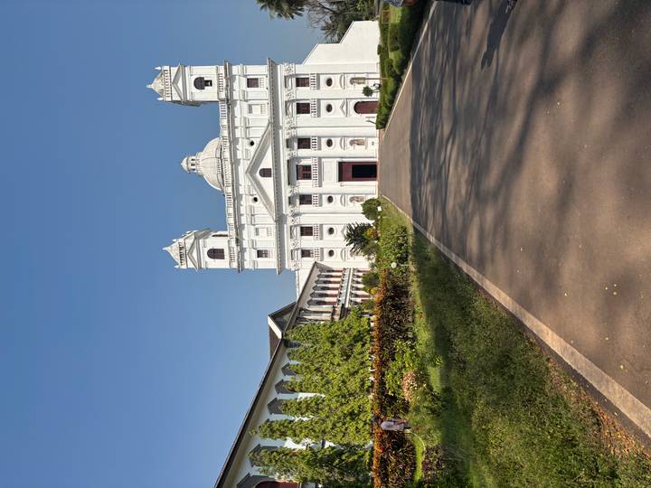 Imposing white church facade surrounded by gardens under clear blue Goa sky