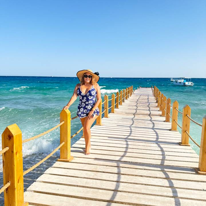 Woman in floral swimsuit posing on a wooden pier stretching into the turquoise Red Sea.