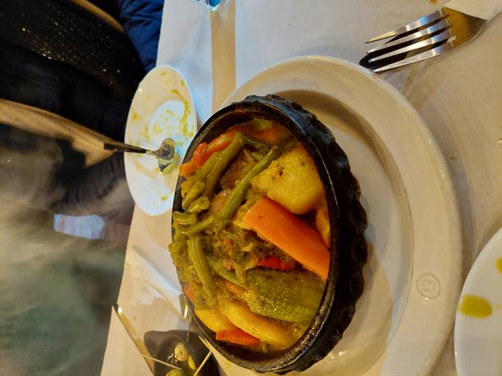 Close-up of a steaming Moroccan vegetable tagine served in a traditional clay pot at a table.