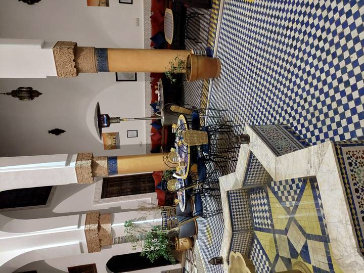 Elegant riad courtyard with mosaic tile floors, columns, lanterns and set dining table in traditional Moroccan style.