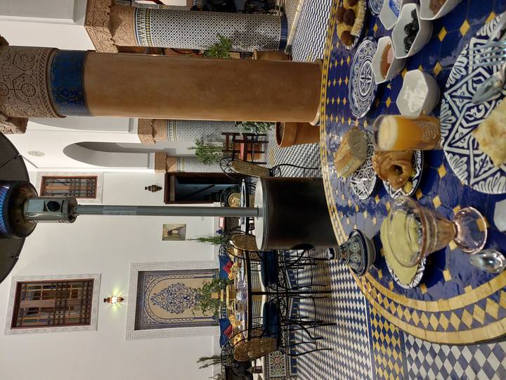 Breakfast spread with juice, pastries and soup on an ornate tiled table inside a Moroccan riad dining area.