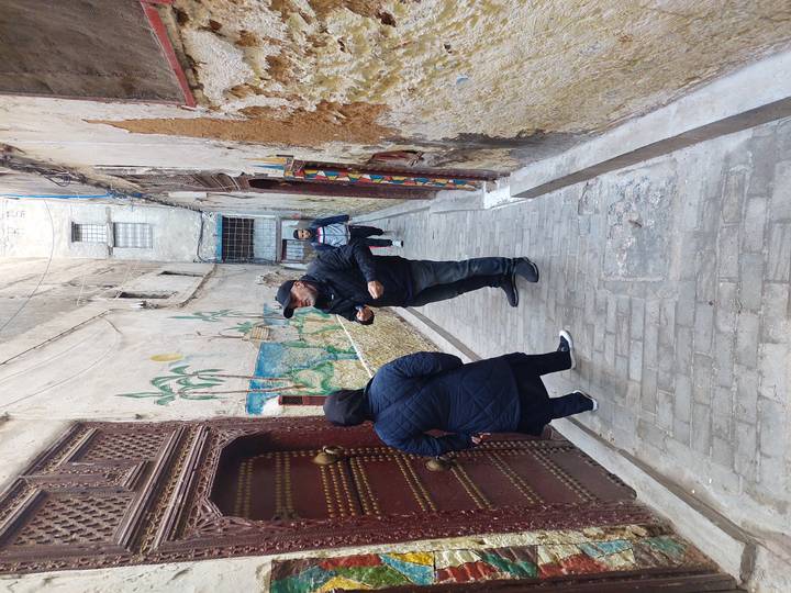 Guide speaks with visitors in a narrow, worn alleyway of an old medina with decorated doors and mural art.