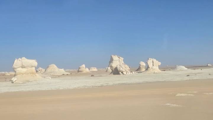 White chalk rock formations rising from flat desert in Egypt's White Desert