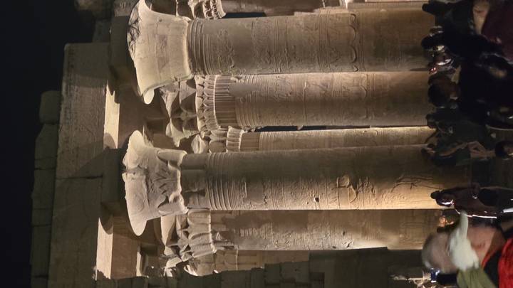 Nighttime view of illuminated columns inside Kom Ombo Temple crowded with visitors