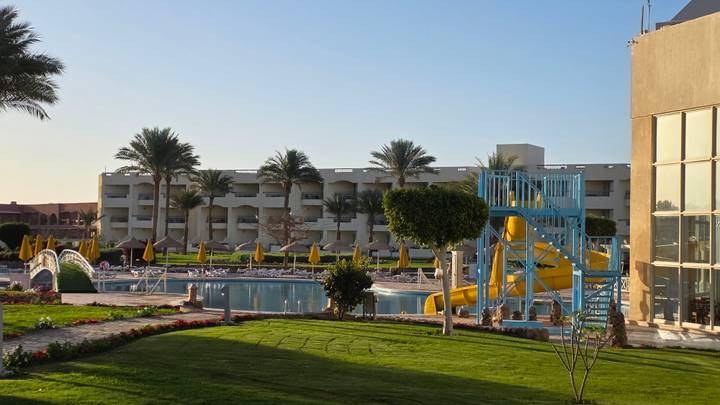 Resort pool area with palms, water slide and modern low-rise accommodation buildings in afternoon light